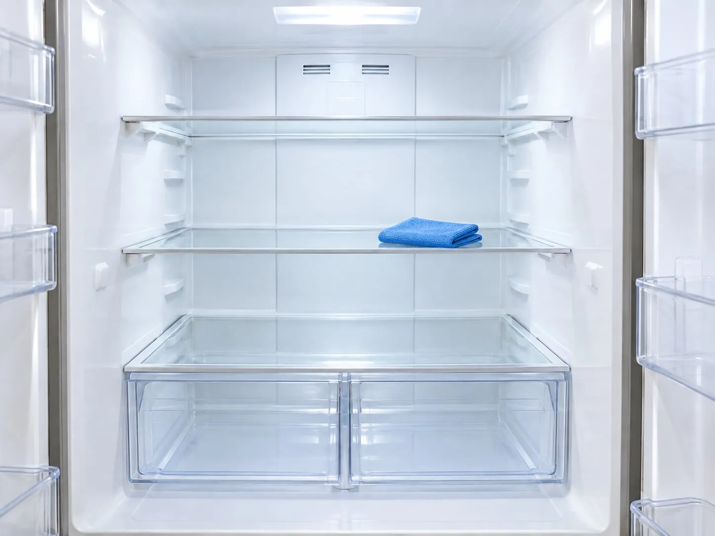 An open, empty and spotless fridge with clear glass shelves